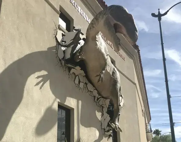 A statue of a t - rex on the side of a building.