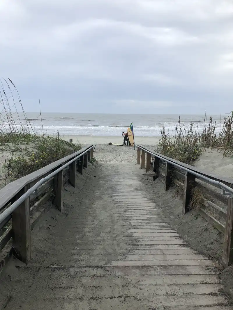 A boardwalk leading to the beach with a person on it.