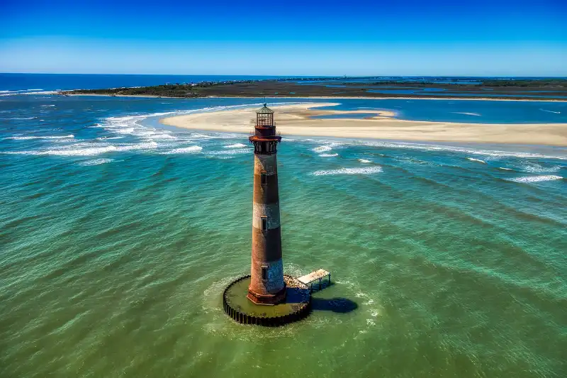 An aerial view of a lighthouse in the middle of the ocean.