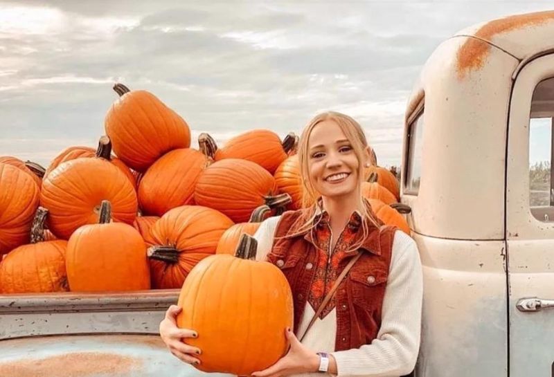 Mini tractor loaded with pumpkins and woman smiling in front