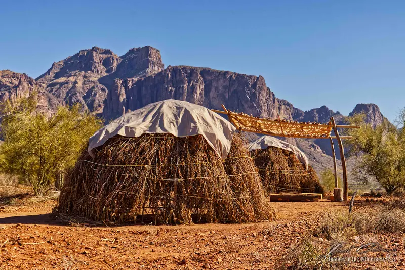 Two huts in the desert with mountains in the background.